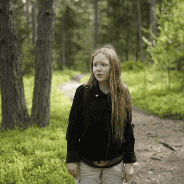 a girl with long red hair stands in the woods