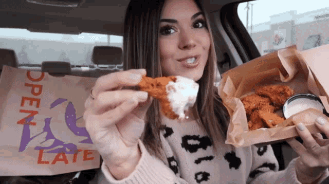 a woman in a car eating chicken wings with a bag that says open late on it