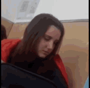 a woman in a red jacket is sitting in a classroom with her eyes closed .