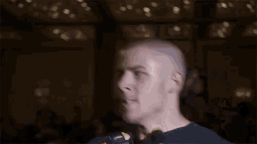 a man with a shaved head is standing in a dark room with a blurred background .