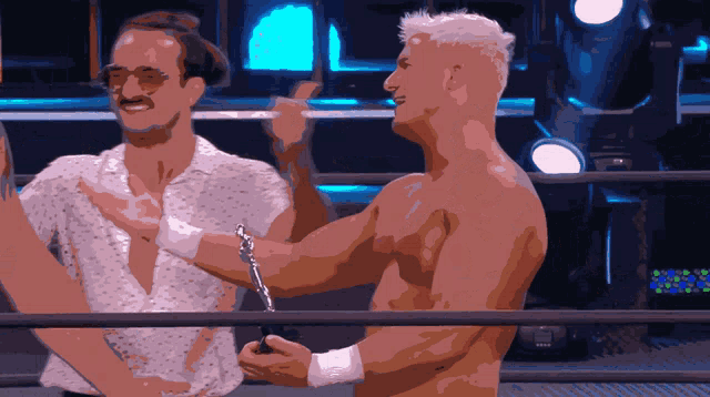 two men are standing in a wrestling ring and one of them has a bracelet on his wrist