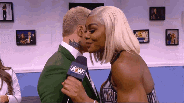a man in a green suit is kissing a woman with a microphone that says aew