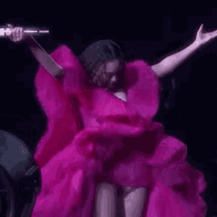 a woman in a pink dress is dancing on a stage in front of a microphone .