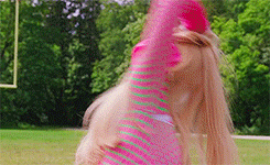 a woman in a pink and green striped shirt is throwing a ball in a field .