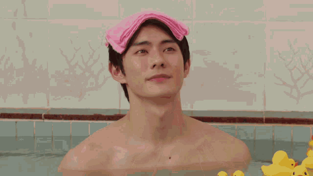 a shirtless man with a pink towel on his head is in a bathtub