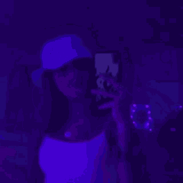 a woman is taking a selfie with a cell phone in a dark room with purple lights .