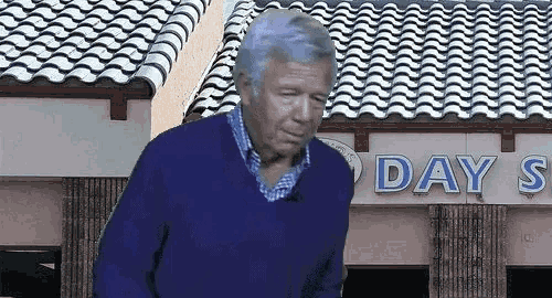 a man in a blue sweater stands in front of a building that says day 's