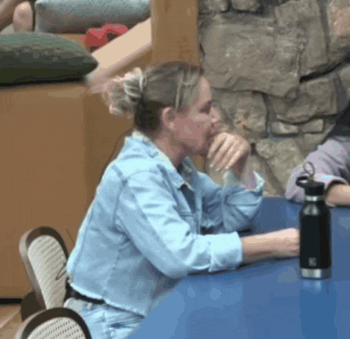 a woman in a denim shirt sits at a table with a black water bottle