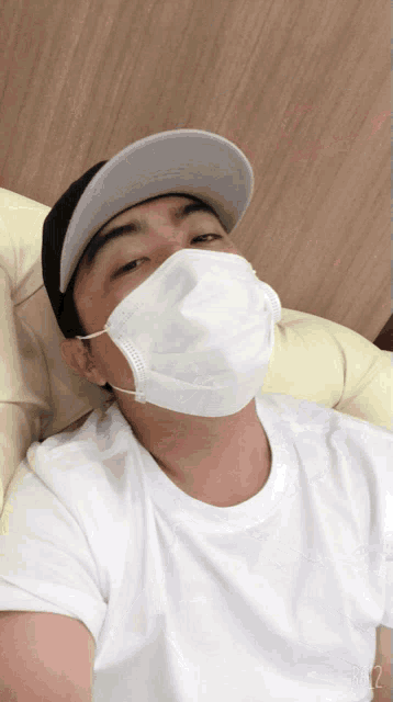 a man wearing a face mask and a hat is sitting on a couch