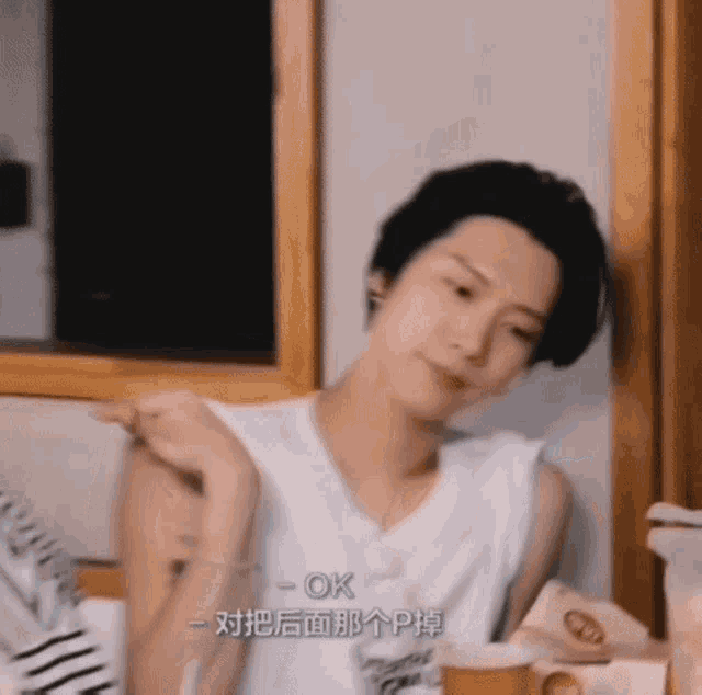 a man in a white tank top is sitting at a table with a cup of coffee in front of him .
