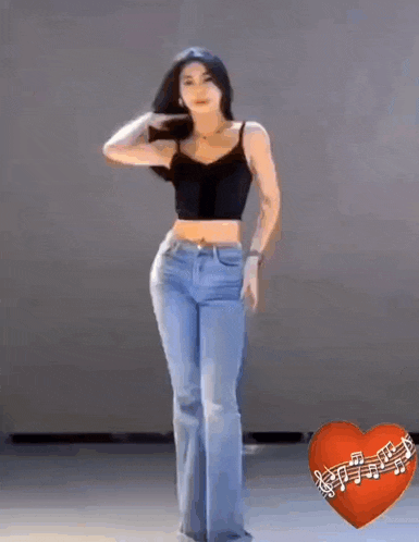 a woman in a black crop top and blue jeans is dancing with a red heart with music notes on it .