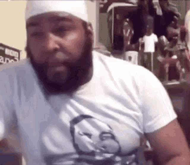 a man with a beard and a white hat is wearing a white shirt .