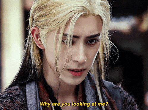 a man with long blonde hair is looking at the camera and says " why are you looking at me "