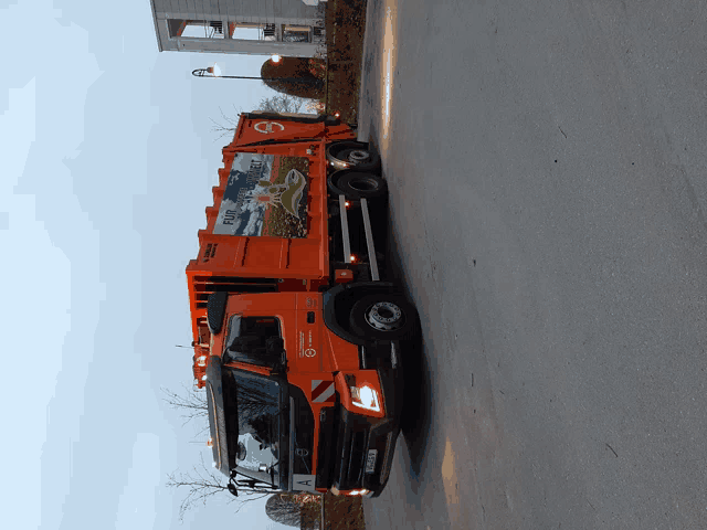 an orange garbage truck is parked on the side of the road and has a sticker on the back that says " volvo "