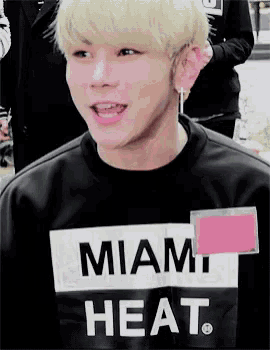 a young man with blonde hair is wearing a black miami heat shirt