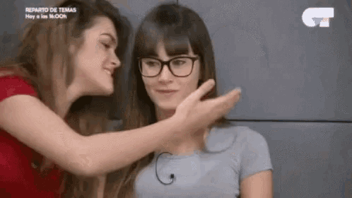 two women are touching each other 's faces while one of them is wearing glasses .