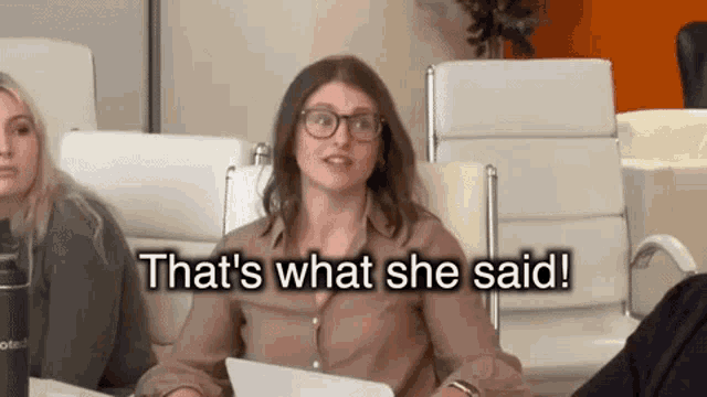 a woman with glasses is sitting at a table with the words that 's what she said behind her