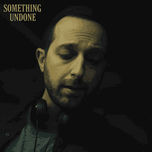 a man wearing headphones looks down with something undone written above him