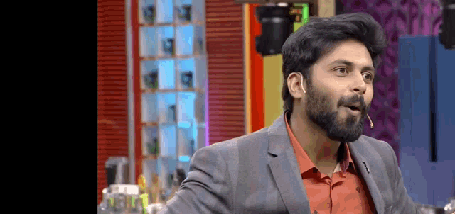 a man with a beard wearing a suit and an orange shirt is standing in front of a microphone .