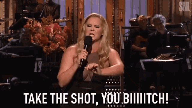 a woman is singing into a microphone and saying take the shot you bitch !