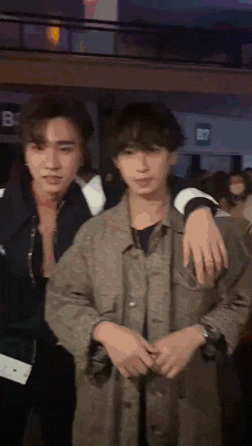 a man with his arm around another man 's shoulder in front of a b7 sign