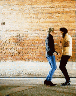 a couple of people dancing in front of a brick wall