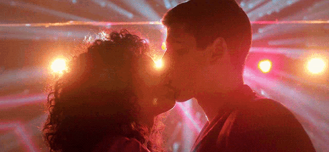 a man and woman are kissing in a dark room with red lights behind them .