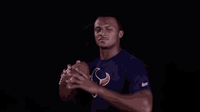 a man in a texans shirt is holding a football in his hand .