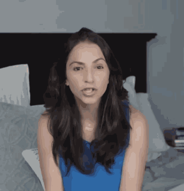a woman in a blue shirt is sitting on a bed talking