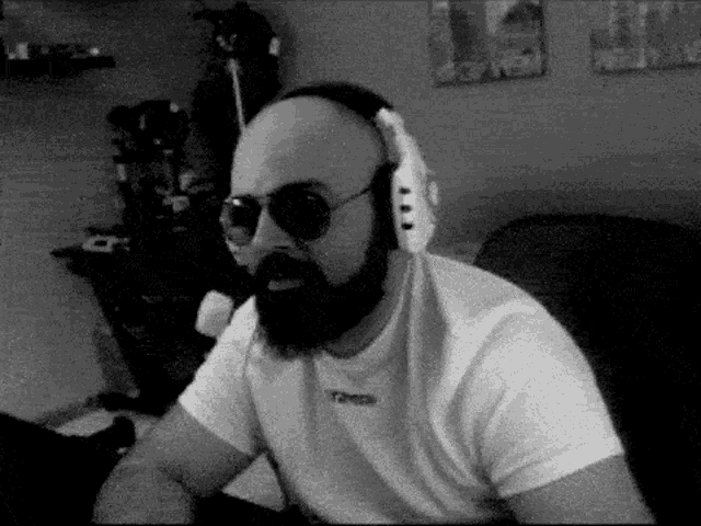 a bald man with a beard and sunglasses is wearing headphones and a white shirt .
