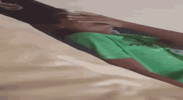 a person in a green shirt is laying on a bed covering their face with their hand .