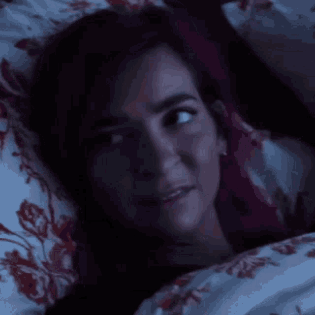 a woman with purple hair is laying in bed with a floral comforter .