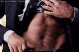 a man in a suit and tie is taking off his shirt to reveal his abs .