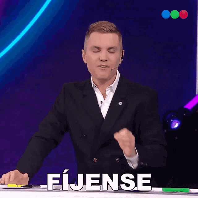 a man in a suit stands in front of a table with the word fijense written on it