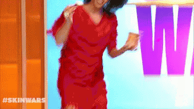 a woman in a red dress is dancing in front of a sign that says ' skin wars ' on it .