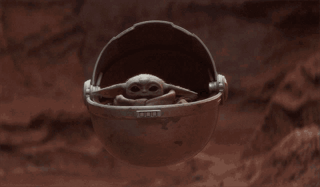 a baby yoda is sitting in a helmet on a brown background