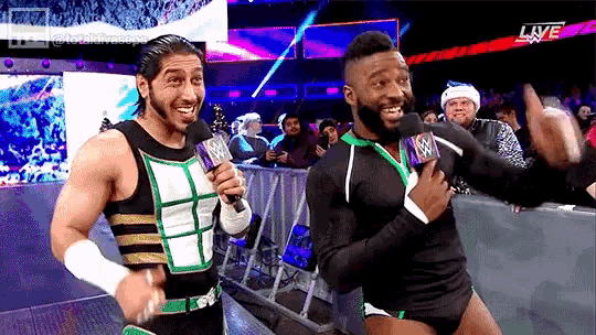 two wrestlers are standing next to each other on a stage and one is holding a microphone with the word live on it