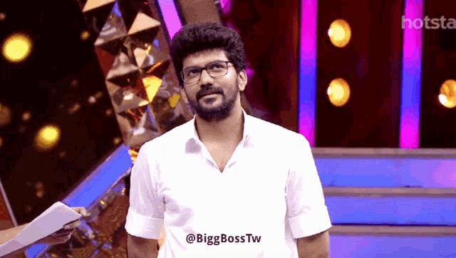 a man with glasses and a beard is standing in front of a hotstar banner