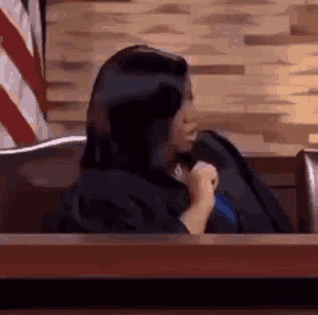 a woman in a judge 's robe is sitting in a courtroom holding a microphone .