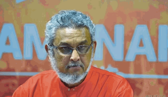 a man with a beard and glasses is sitting in front of a sign that says amnai