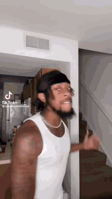 a man in a white tank top with a headband on his head is standing in a room .