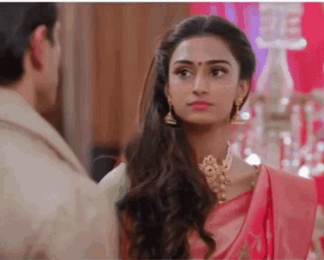 a woman in a pink saree and gold jewelry is looking at a man in a suit .