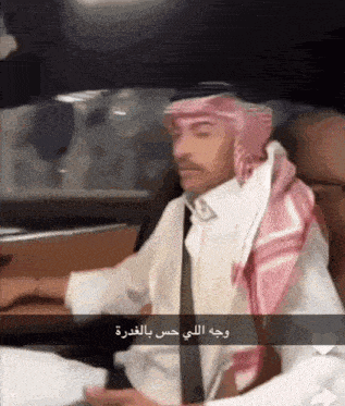 a man wearing a head scarf and a white shirt sitting in a car