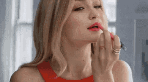 a woman is applying lipstick to her lips while looking at herself in the mirror .