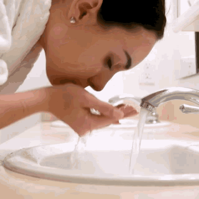 a woman is washing her face in a sink with water running from the faucet