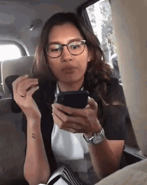 a woman wearing glasses and a watch is looking at her cell phone
