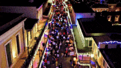 an aerial view of a crowd of people walking down a street with christmas lights