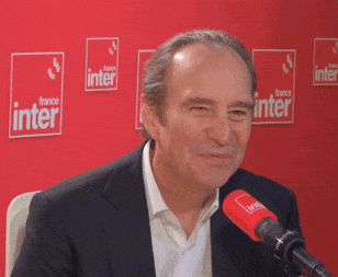 a man sitting in front of a microphone with a france inter sign in the background