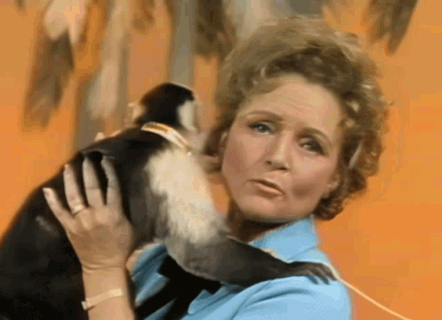 a woman in a blue shirt is holding a black and white monkey on her shoulder