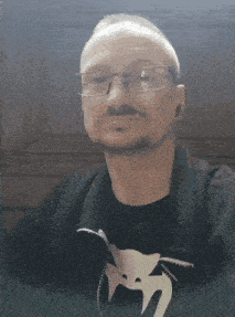 a man wearing glasses and a black shirt with a snake on it looks at the camera